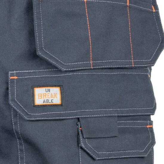 Close-up of a dark gray fabric pocket on the Unbreakable U230 Kestrel Holster Black Shorts, featuring orange and white stitching and a label that reads UNBREAKABLE with BREAK in bold orange. Part of the U230 collection.