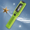 A green handheld LED work light with a black button is angled on a blue background, next to a gold star and white, sparkling light trails.