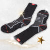 A pair of black and gray socks with red accents and geometric patterns is displayed on a light surface. The socks have a ribbed upper section. Decorative sparkles and a gold star are placed nearby.