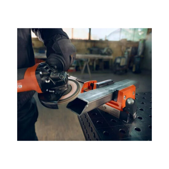 A person wearing black gloves uses an angle grinder to work on a metal piece secured in an orange metal vise on a workbench in a workshop.