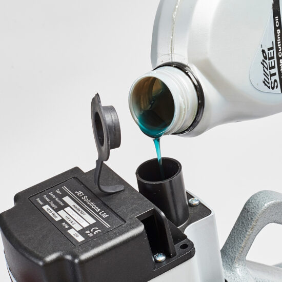 A close-up of blue oil being poured from a bottle into a black oil reservoir of a machine, with a flipped-open cap and a label visible on the machine component.