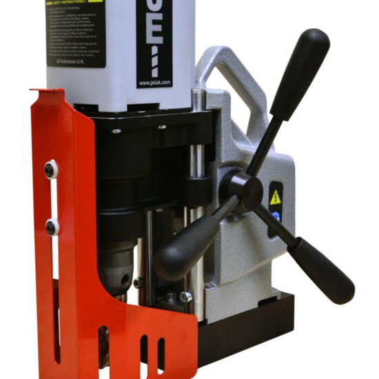 Close-up of a magnetic drill press with a red safety guard, three black handles, and a metallic frame, used for drilling precise holes in metal surfaces.