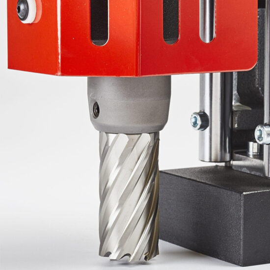 Close-up of the cutting head and drill bit of a red industrial drilling or milling machine, showing the metal bit and part of the machines frame.