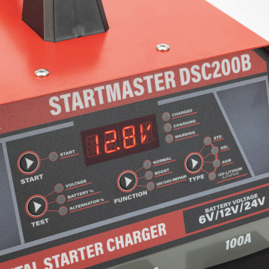 Close-up of a Startmaster DSC200B metal starter charger showing its digital display reading 12.81, along with various buttons, lights, and labels indicating charger settings and battery types.