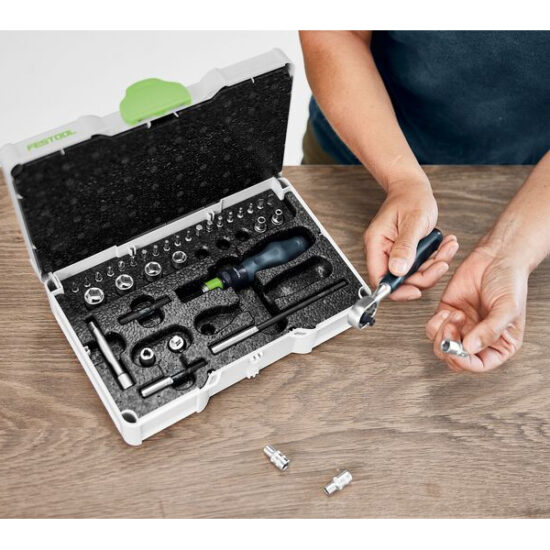 A person’s hands work on a metal tool part over a wooden table, next to an open foam-lined toolkit with screwdriver bits and attachments, beside a Festool Air Purifier SYS-AIR M.