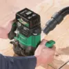 A person uses the green and black Hikoki HIKM3612DAJP M3612DA/JPZ 1/4 & 1/2in Multi-Volt Router 36V 2.5Ah Li-ion with a hose to carve a groove in plywood, delivering efficient, precise results.