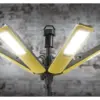 A close-up of the Firthfull FPPCENTAURL Centaur Heavy-Duty LED Site Light, 200W 110V, showing its six yellow rectangular panels and central black stand, illuminated against a blurred brick wall background.