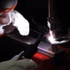 Wearing white protective gloves, a user welds metal pieces in a workshop with bright sparks using the Lorch MicorTIG 200 BasicPlus.