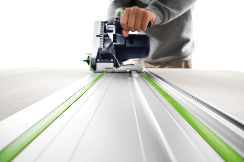 A person operates a circular track saw, guiding it along a metal rail to make a precise cut in a wooden board. The focus is on the saw and track, with the users hand holding the saw handle.