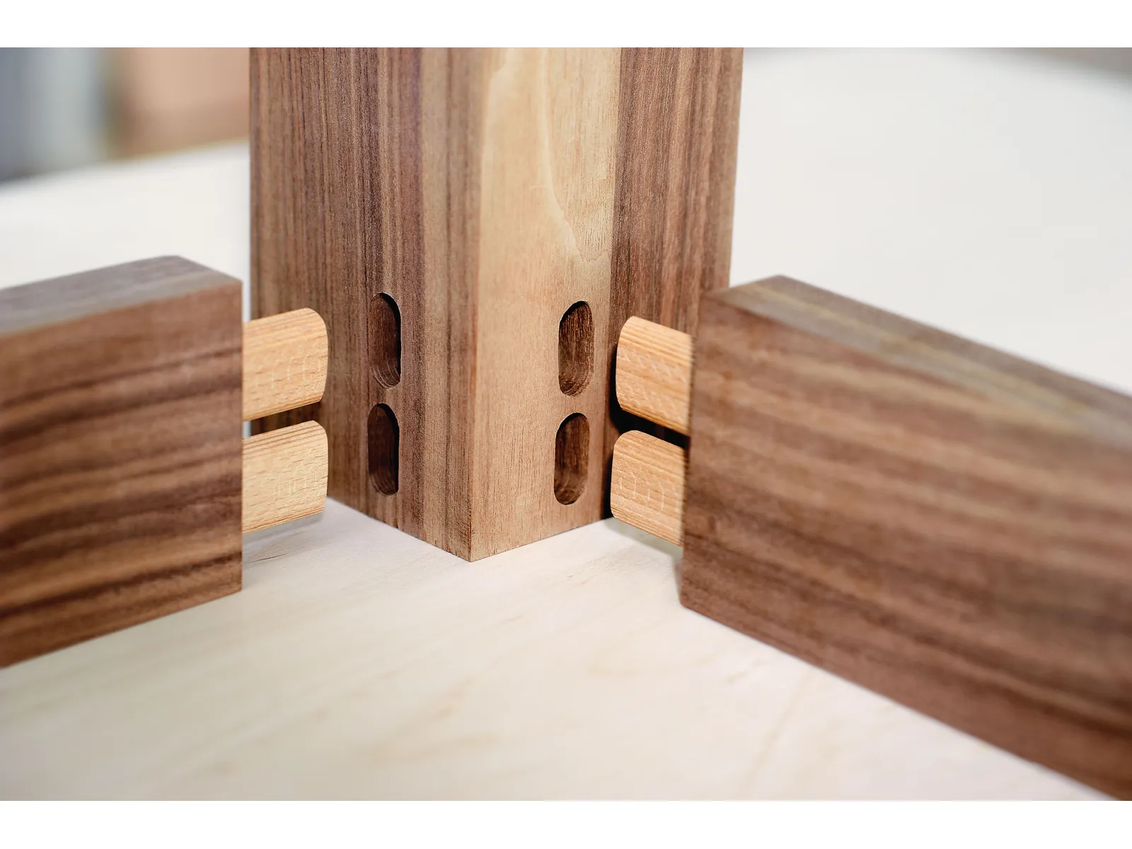 Close-up of wooden pieces with two light-colored Domino Beech tenons ready to fit into matching mortises in a vertical wood piece.