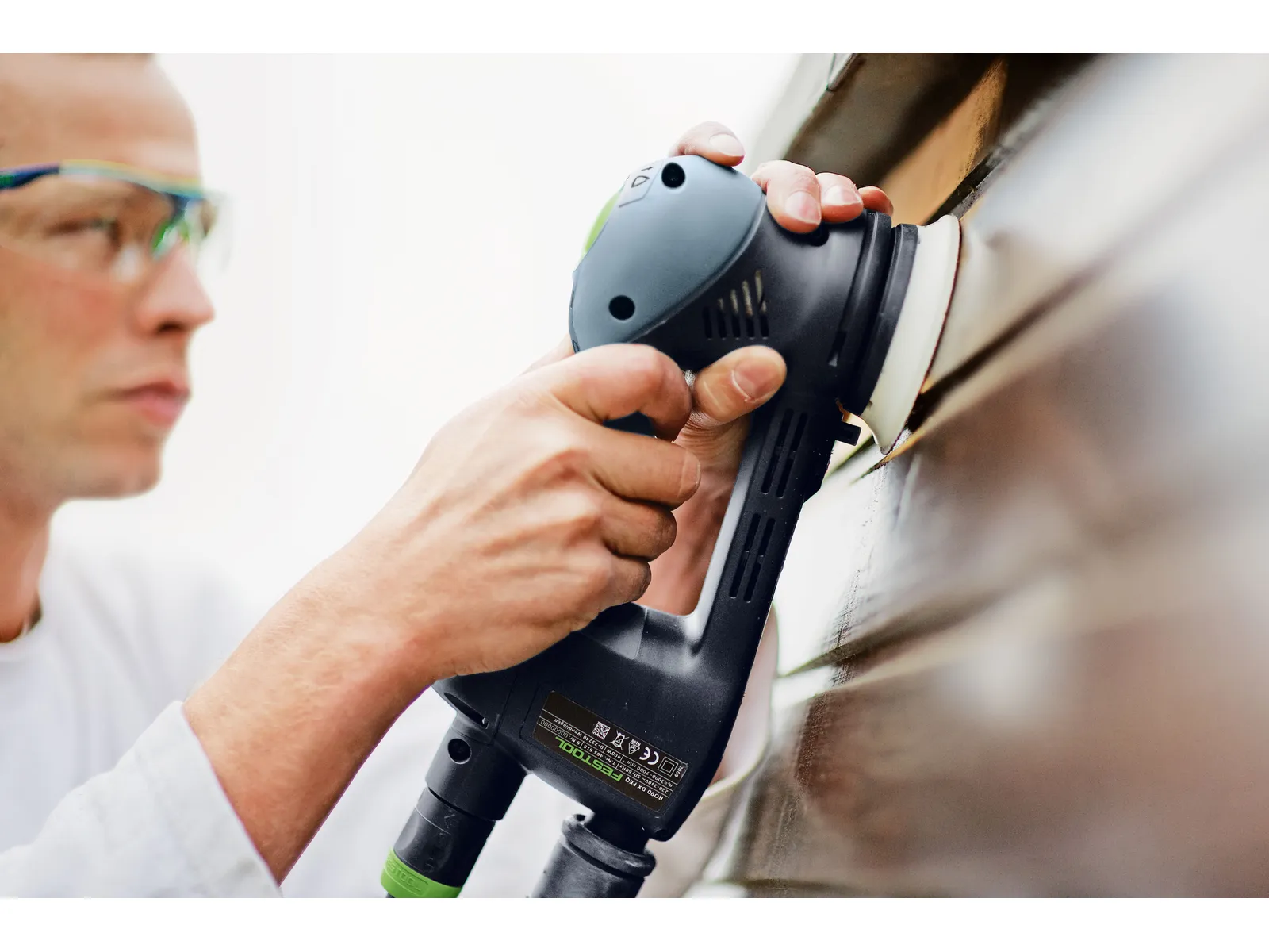 A person in safety glasses uses Festool 498214 10x80 Domino, Beech, carefully joining wood pieces with precise handwork.