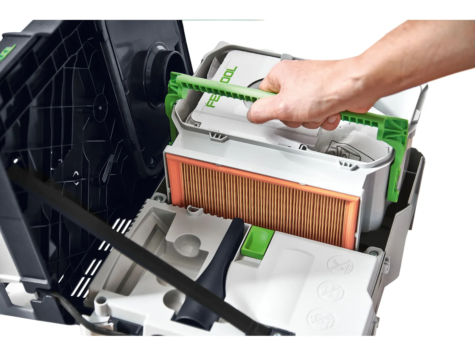 A hand lifts a green handle in a vacuum cleaner, revealing an orange filter and white dust bag; the open lid shows its internals.