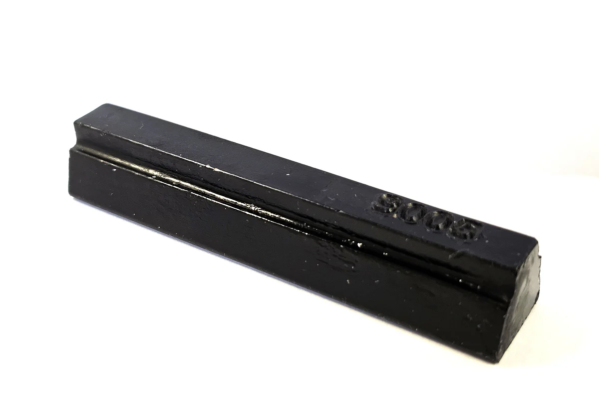 A black rectangular bar with a smooth surface and a small raised marking on one end is placed on a white background.
