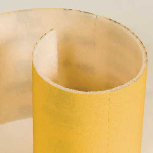 A close-up of a Mirka Goldflex Soft 115 x 125 mm Perforated Roll, P320 200PC, partially unrolled to reveal its textured abrasive surface and smooth backing.