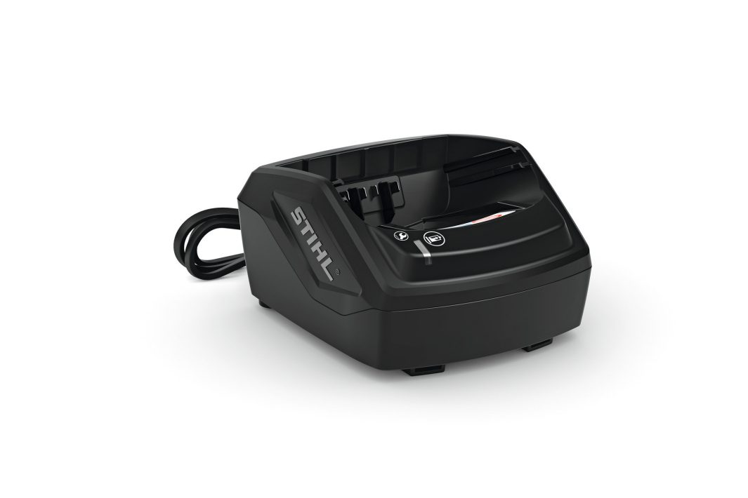 A black STIHL battery charger sits on a white surface with a power cord extending from the back and a slot for charging in front.