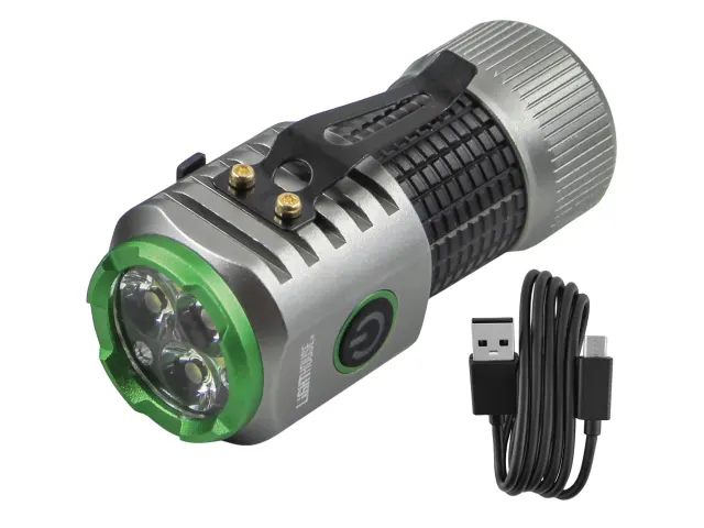 A compact silver and black flashlight with a green-rimmed lens sits next to a black USB charging cable, featuring a clip and power button.