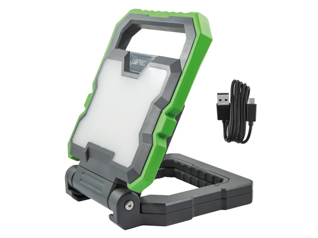 A portable, rugged green and gray LED work light with a folding stand, placed beside a black USB charging cable.