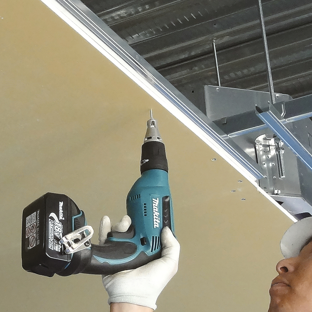 A person in a white glove uses a teal cordless drill to secure a screw into a ceiling panel beneath a metal frame.