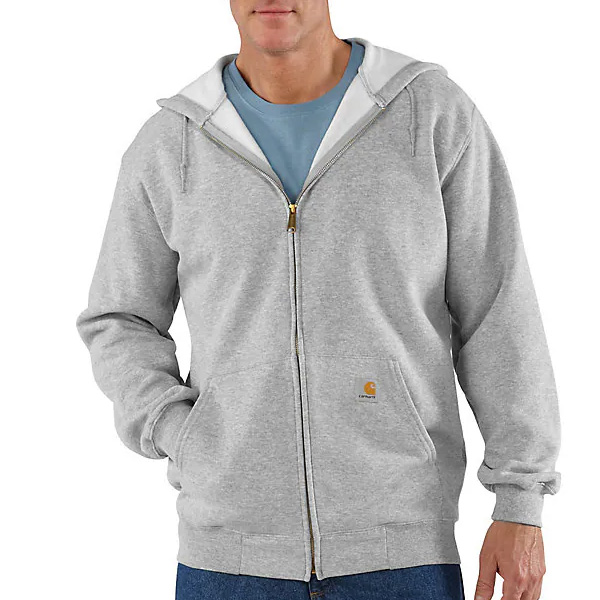 A man wears a gray Carhartt hoodie over a blue t-shirt and blue jeans, with hands in front pockets and a small logo on the hoodie.