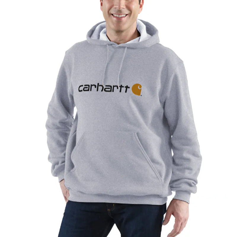 A smiling person wears a black Carhartt sweatshirt with a front pocket and the classic logo graphic across the chest.