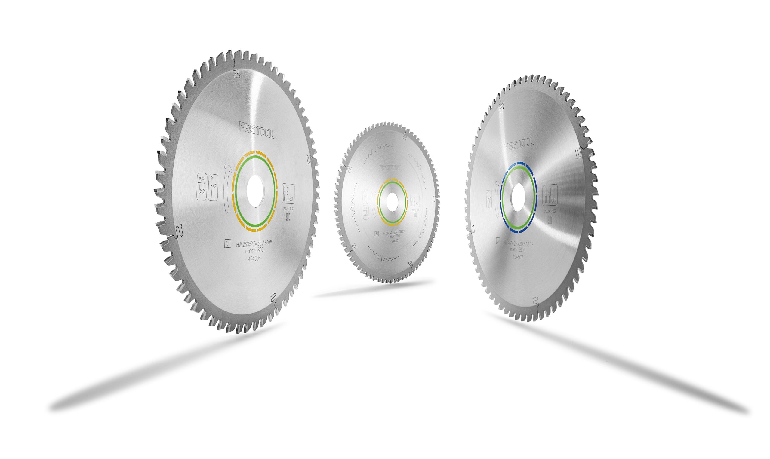 Three Festool 578570 saw blades with sharp teeth and colored rings stand upright on a white surface, casting long shadows.