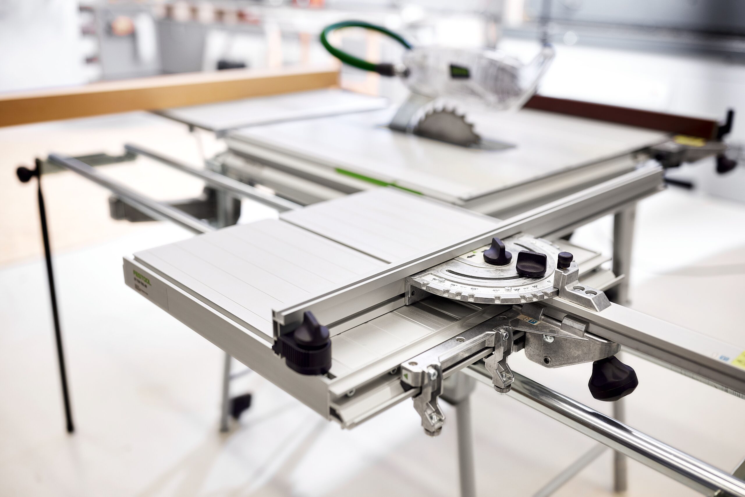 A close-up of the Festool 578099 Sliding Table ST 840 TKS 80 shows its guide fence, measuring scales, saw blade, and knobs in a workshop.