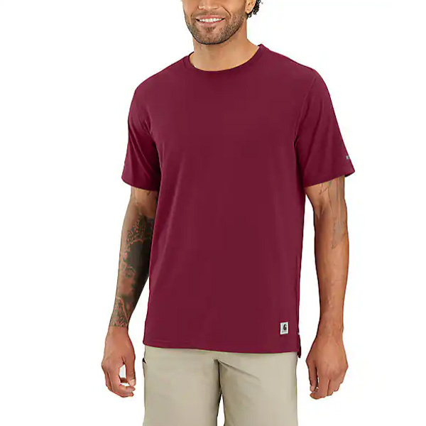 A man smiles in a relaxed fit Carhartt Carbon Heather T-shirt and light khaki shorts, showing right forearm tattoos on white.