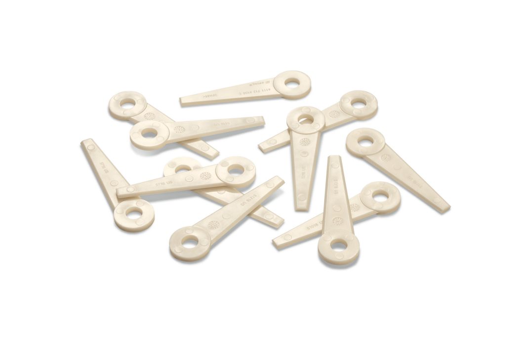 Several beige plastic levers with circular holes at one end are scattered on a white background.