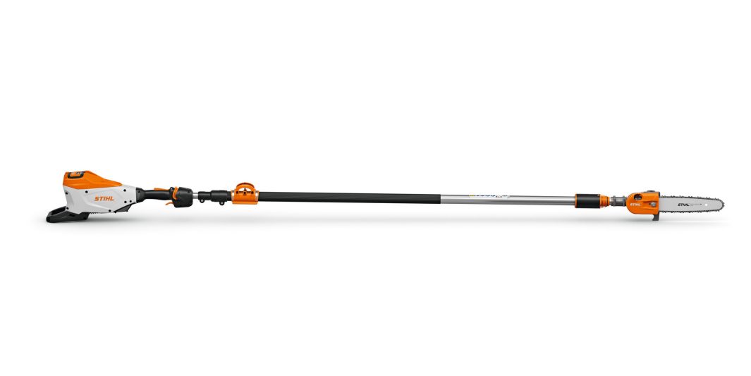 A STIHL battery-powered pole pruner with orange and white motor housing, long black shaft, and chainsaw blade for trimming high branches.