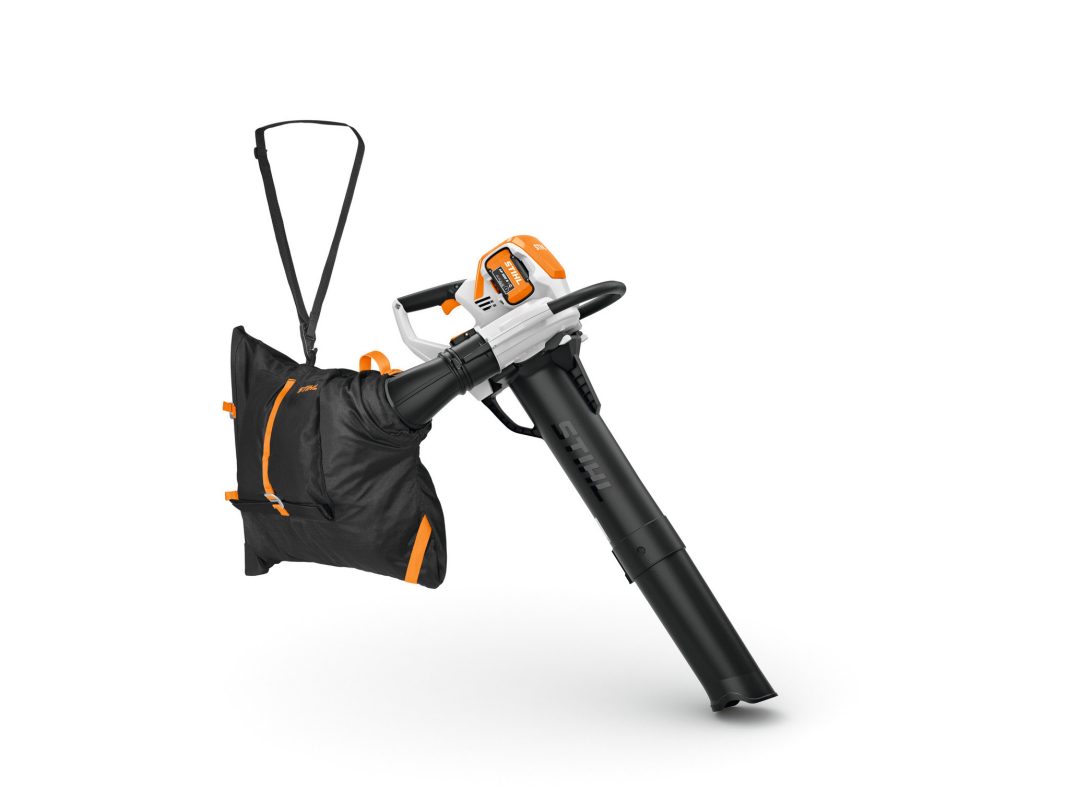 A handheld orange and black leaf blower with a shoulder strap and attached collection bag, displayed on a white background.