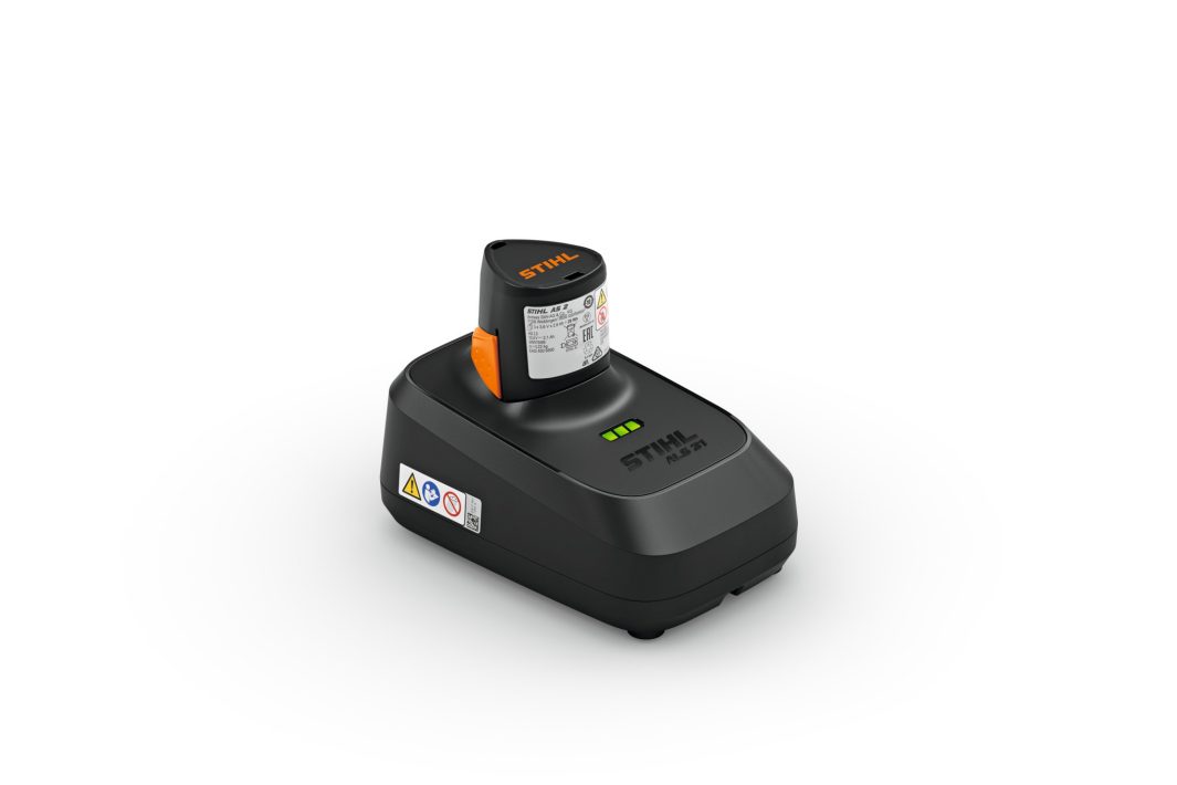A black STIHL battery charger with an attached battery, featuring indicator lights and warning labels, on a plain white background.
