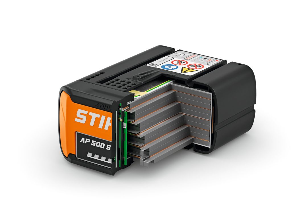 A close-up of a black and orange STIHL AP 500 S battery with the side open, showing internal cells and safety labels on top.