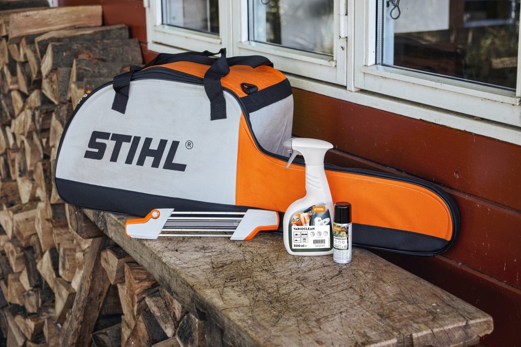 A Stihl Chainsaw Carry/Storage Bag on a wooden bench by stacked firewood, with tools and spray in front near a windowed wall.